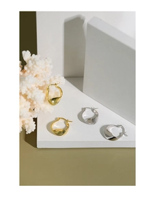 Dettaglio di orecchini a cerchio ritorti minimalisti in oro e argento su corallo bianco