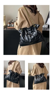 Close-up of black quilted bucket bag featuring golden chain strap and drawstring closure