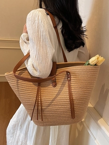 Large woven straw tote bag with brown handles, held by a model for a casual beach look