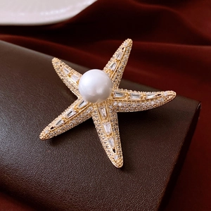 Close-up of 14K gold-plated starfish brooch with white pearl and zircon on brown leather