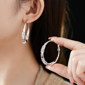 Close-up of silver twisted hoop earrings with sparkling rhinestones on a female model