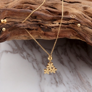 Close-up of 18K gold daisy flower pendant necklace and stud earrings set on wood texture