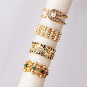 Detailed view of four gold-plated rings featuring pearls and vibrant gemstones on a stand