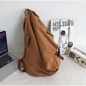 Detailed view of brown washed canvas backpack with unique folded design on white bedding