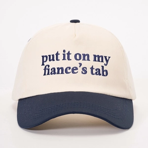 Detail of navy blue embroidery saying 'put it on my fiance's tab' on a beige baseball cap