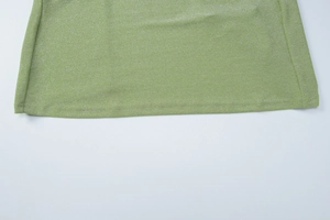 Close-up of sparkling grass green knitted fabric with shimmering texture and side slit detail