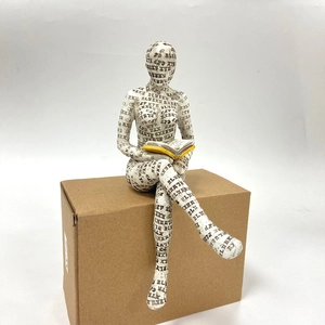 Detail of reading woman resin statue with newspaper print and yellow book decor