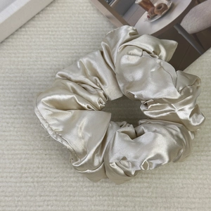 Close-up of a premium oversized champagne satin silk scrunchie with soft fabric pleats