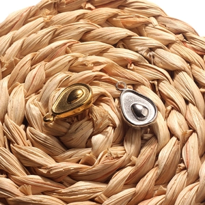 Detailed close-up of gold and silver avocado metal pendants on a woven straw background
