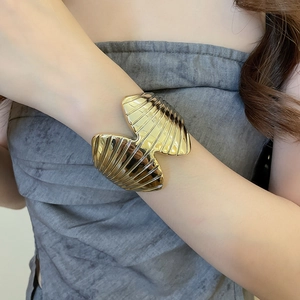 Detailed view of a wide gold metal open cuff bracelet with wavy textured shell pattern
