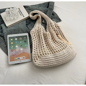 Beige woven knit tote bag with tassel detail styled on white fabric with casual items