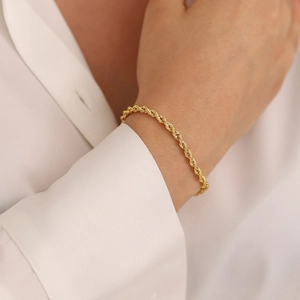 Detailed view of 18K gold plated rope chain bracelet worn on a female wrist over white shirt