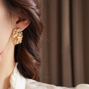 Close-up of irregular textured gold earrings featuring a lava-like molten metal design
