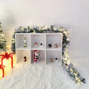 Flocked Christmas garland with LED lights, silver ornaments and pine cones on white cabinet