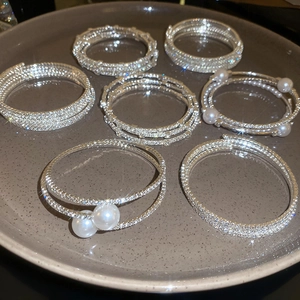 Dettaglio di bracciali elastici argento a più strati con strass e perle sintetiche