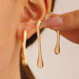 Modern gold liquid teardrop earrings with a polished metallic finish on a model