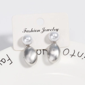 Detail view of pearl stud earrings with silver brushed metal pendants on a jewelry card