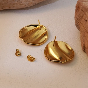 Detailed close-up of golden irregular wavy disk earrings with liquid metallic finish