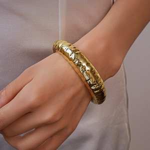 Close-up of a chunky 18K gold-plated hammered texture bangle on a silky background