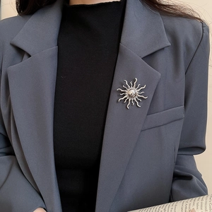 Silver sun-shaped brooch pinned on dark grey suit lapel showing luxury metal texture