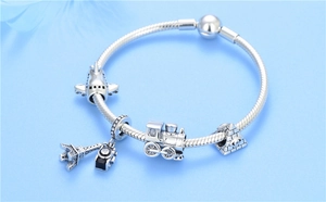 Detail of S925 silver charm bracelet featuring travel charms like the Eiffel Tower and plane