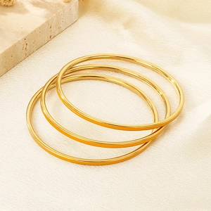 Detail showing set of three 3mm polished gold stainless steel bangles on fabric