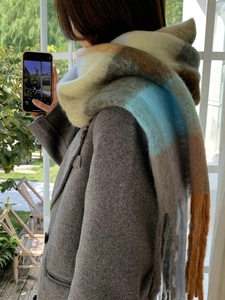 Model wearing a thick plaid rainbow check scarf with tassel edges in a sunlit window