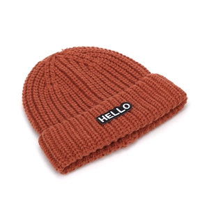 Gros plan du bonnet en tricot rouge brique avec écusson HELLO et texture en maille