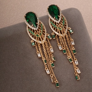 Close-up of gold dangle earrings with emerald green teardrop stones and tassels