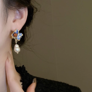 Close-up of vintage irregular earrings with blue enamel and baroque pearls on model