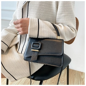 Model wearing a stylish black leather square crossbody bag with decorative oversized buckle