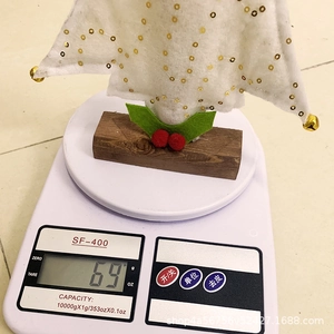 Mini white felt Christmas tree with golden sequins on a scale showing 69g weight
