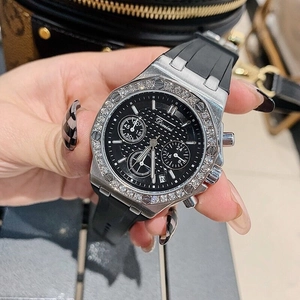 Detailed close-up of a silver rhinestone watch with black rubber strap and chronograph dial