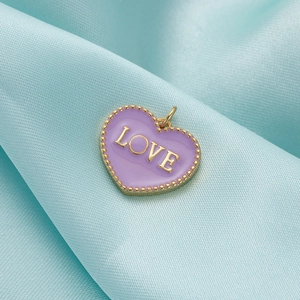 Detailed macro shot of a heart-shaped purple enamel LOVE pendant on blue silk fabric