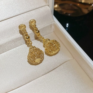 Macro shot of gold hollow lantern drop earrings resting on beige silk lining