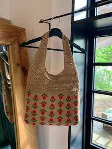 Detail of hand-crocheted beige tote bag with red floral pattern and openwork knit