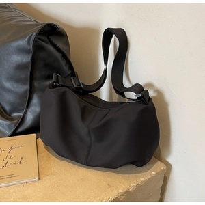 Close-up of black nylon crescent tote bag with wide strap on minimalist stone surface