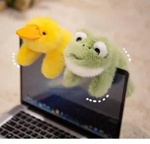 Cute plush duck and frog dolls hanging on a laptop screen as creative office decor