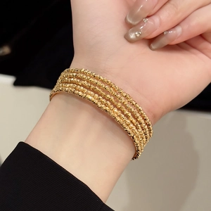 Detail of four layered gold plated textured bracelets on wrist with minimalist metallic beads