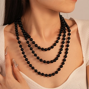 Close-up of triple-layered black round bead necklace styled on a white sweater