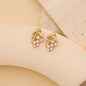 Macro detail of gold floral shell earrings with white pearls on a stone backdrop