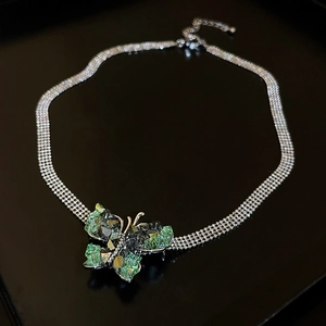 Macro view of silver butterfly pendant with green and black crystals on a reflective surface