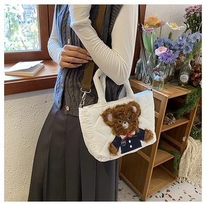 Detail of white quilted handbag with a brown plush teddy bear accent and shoulder strap