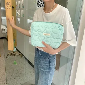 Quilted mint green cosmetic bag with heart embroidery held by a model in a casual setting