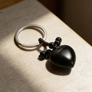 Polished black obsidian heart pendant keychain with woven cord on stone surface