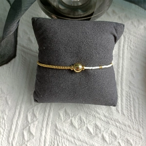 Detail of beaded bracelet with gold beads and white pearls on a grey display pillow