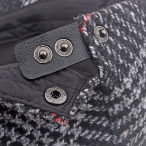 Nahaufnahme der Tweed-Mütze mit verstellbarem Lederriemen und geprägten Metalldruckknöpfen