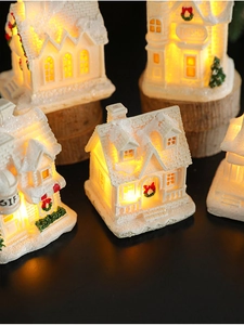 Close-up of a resin LED Christmas snow house with warm lights on a rustic wood base