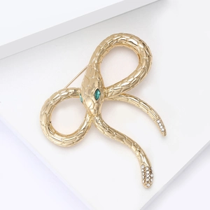 Golden snake brooch with green gemstone eyes and rhinestone tail on white stand
