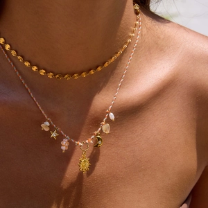 Dettaglio di collana a strati con ciondoli sole e luna, perle e cordino intrecciato oro